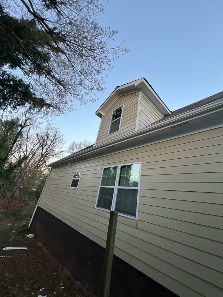 Two-story house with beige siding, elevated on dark foundation, featuring a peaked roof cupola and large windows on a clear day