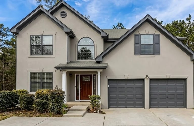 Two-story beige house with dark garage doors, red front door, multiple windows, and landscaped front yard