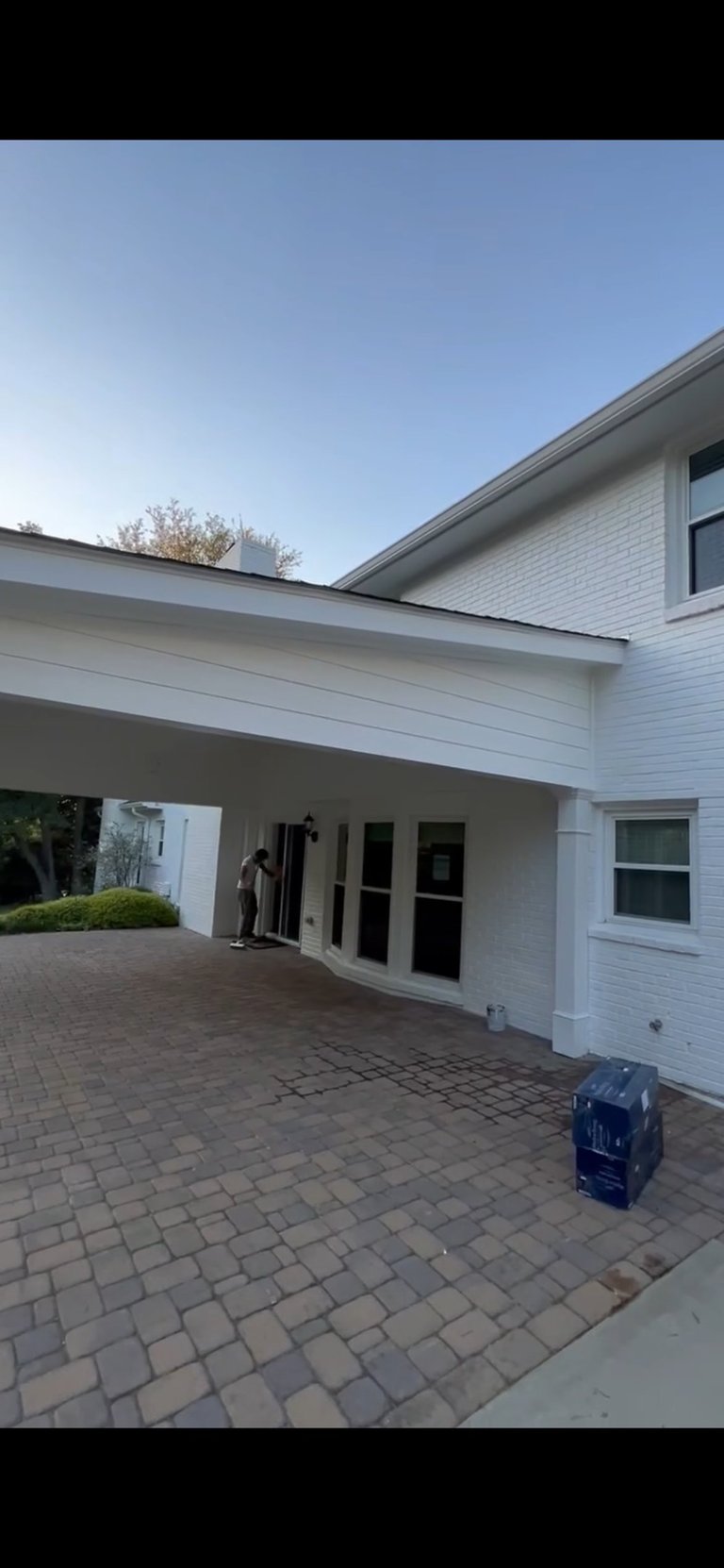 Modern white house with covered carport, brick driveway, and blue luggage on pavement