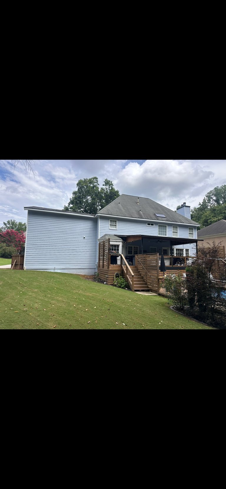 Two-story white house with garage addition, wooden deck, and manicured lawn under partly cloudy sky