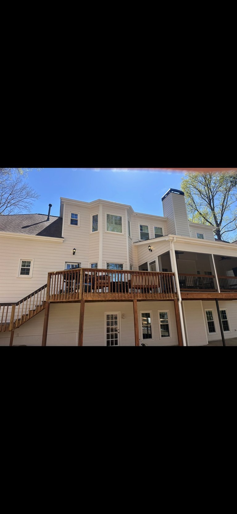 Multi-level cream-colored residential house with wooden decks and railings under blue sky with bare trees