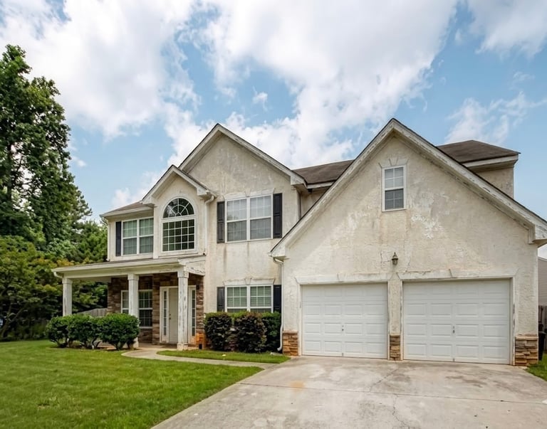 Two-story beige house with double garage, front porch, and manicured lawn on a sunny day