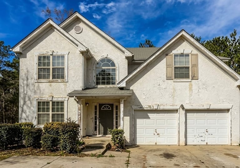 Two-story white suburban house with brick accents, double garage, front porch, and landscaping under blue sky